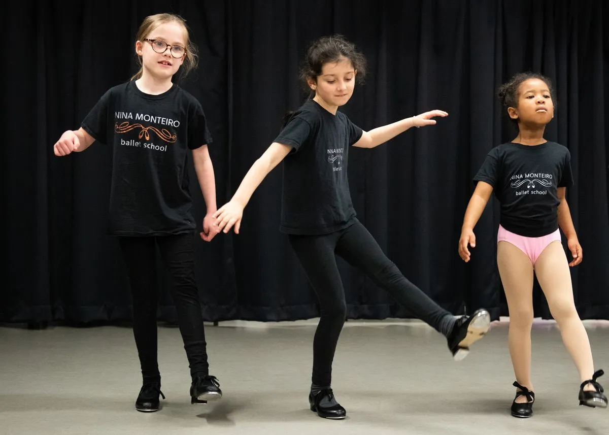 Three young dancers holding hands while practicing tap steps together